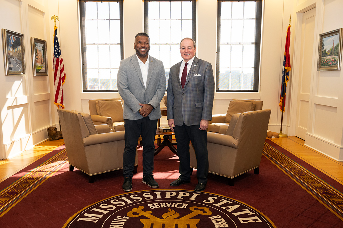 Two men in blazers standing in sitting room with maroon rug and seal