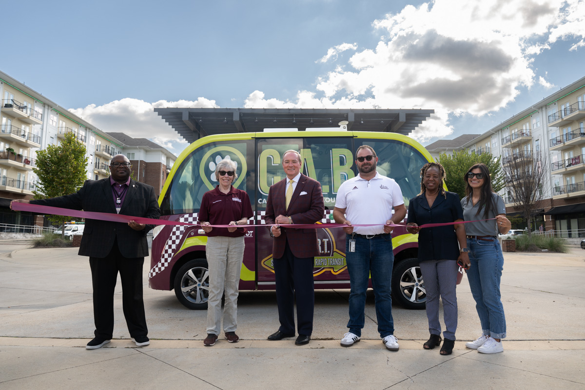 Officials stand in front of electric-autonomous shuttle for ribbon cutting